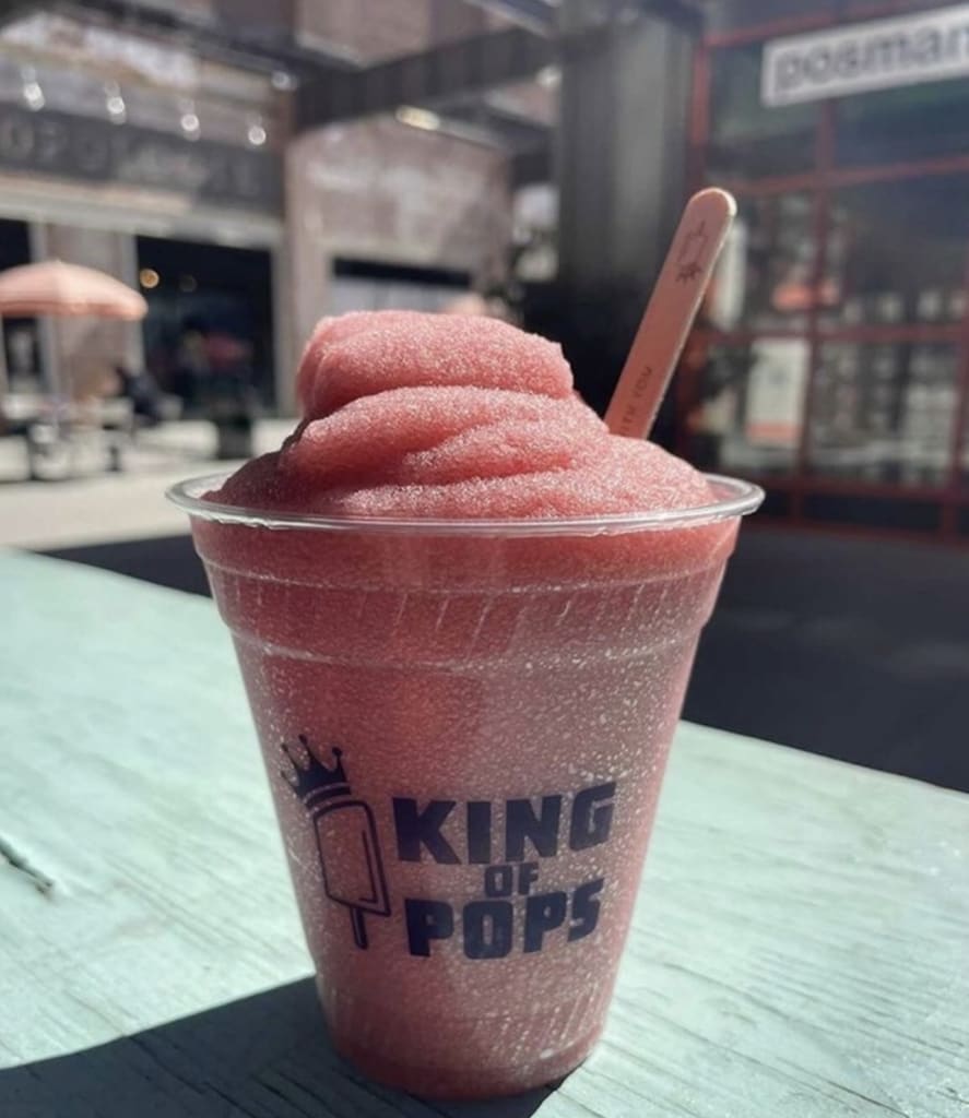 Bebidas de Verano en Atlanta 4 A pink frozen drink with a crown logo sits on a wooden table outside in Atlanta, Georgia.