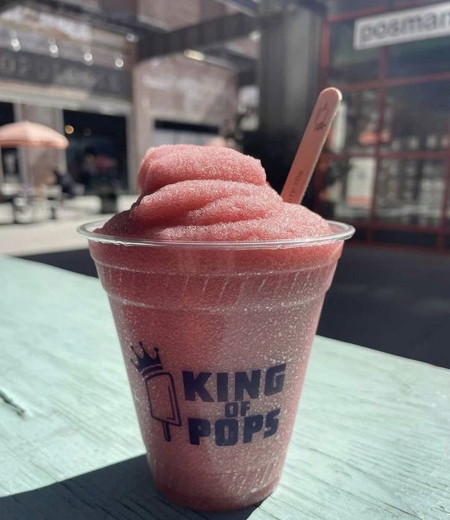Must-Try Summer Cocktails in Atlanta 8 A pink frozen drink with a crown logo sits on a wooden table outside in Atlanta, Georgia.