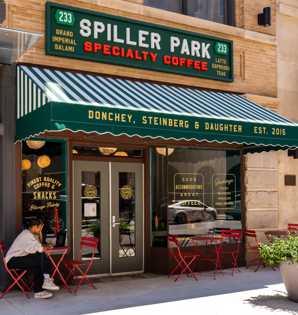 A person sits at a red table outside a coffee shop with a green awning in Atlanta, Georgia.