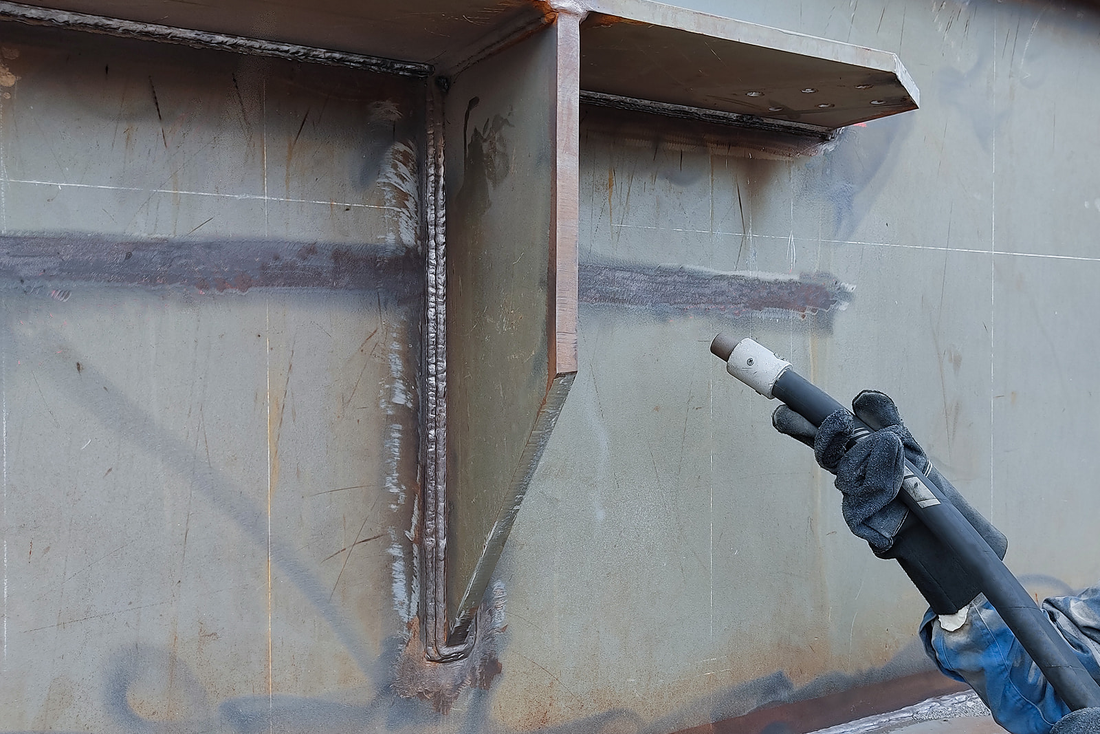 Technician sandblasting welded steel surfaces for industrial coating preparation in Appleton, WI.