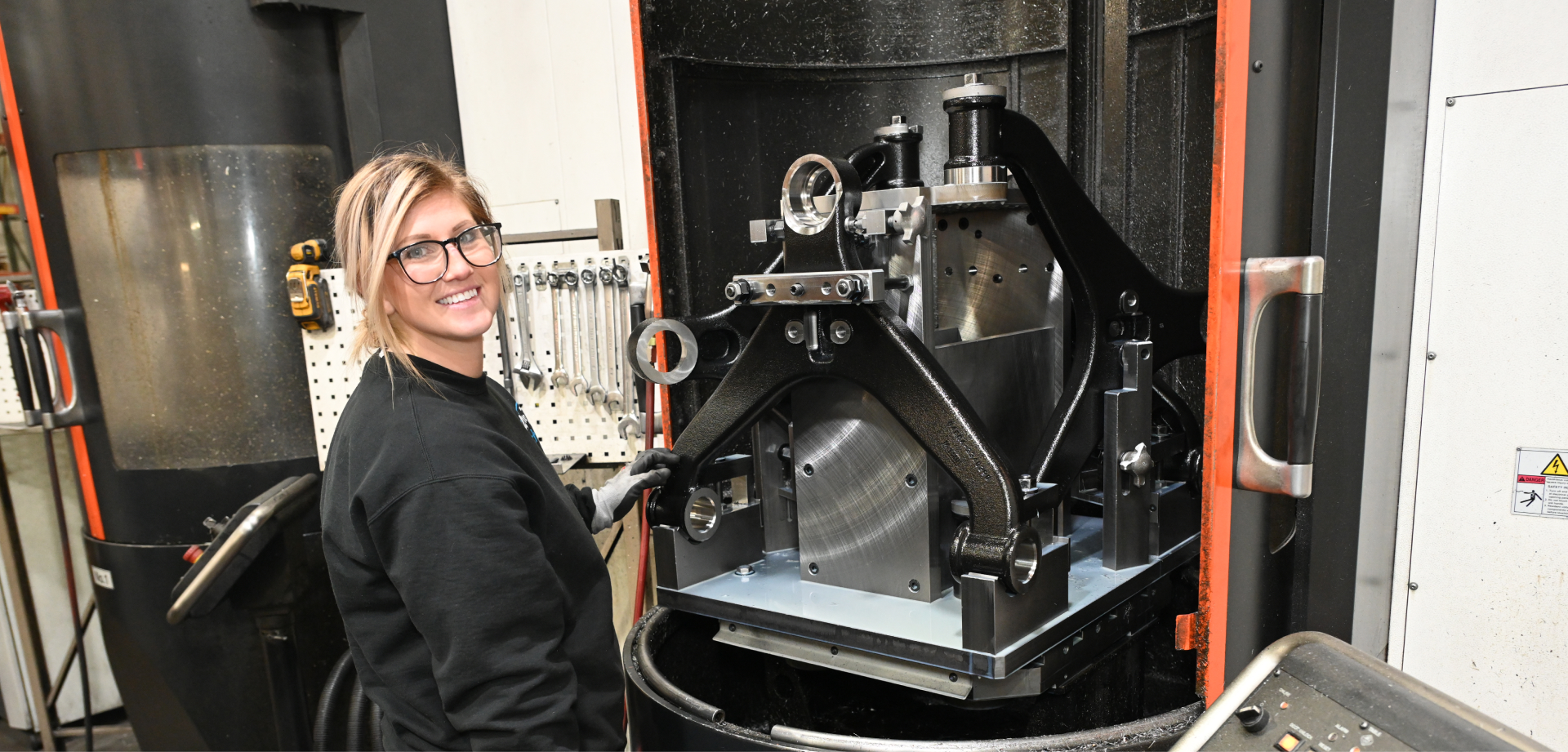 A woman wearing glasses stands confidently in front of a large machine