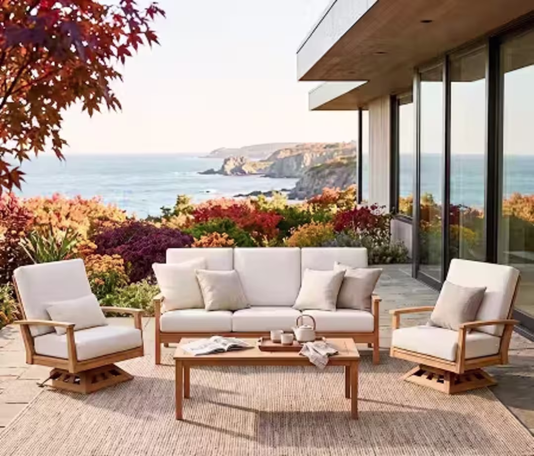 Cushioned outdoor sofa and two lounge chairs surround a teak coffee table on an autumn coastal patio.