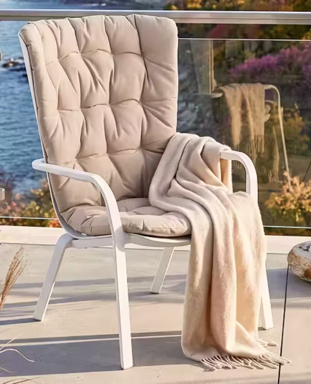 Tufted outdoor chair cushion with a soft throw blanket draped over the arm on a coastal patio.