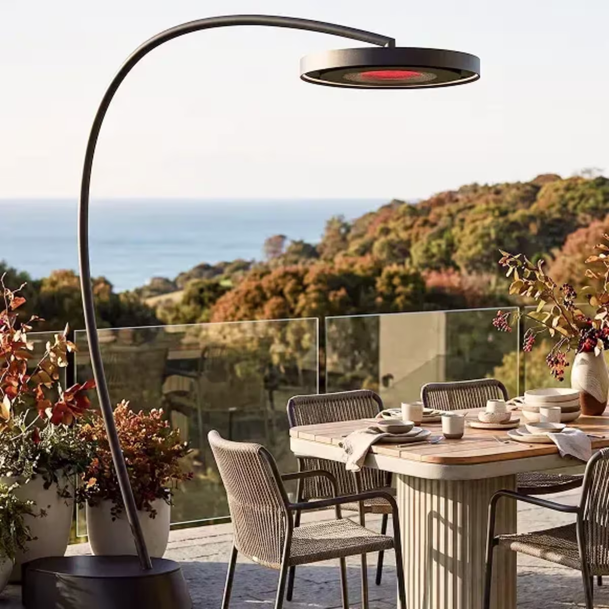 Arched freestanding patio heater over an outdoor dining table with woven chairs.
