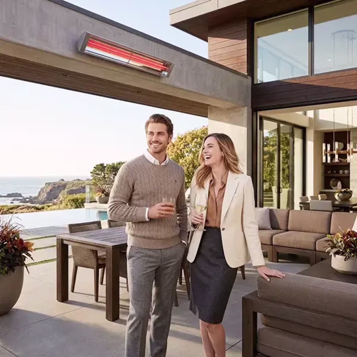 Couple standing beneath a wall-mounted patio heater on a modern coastal patio.