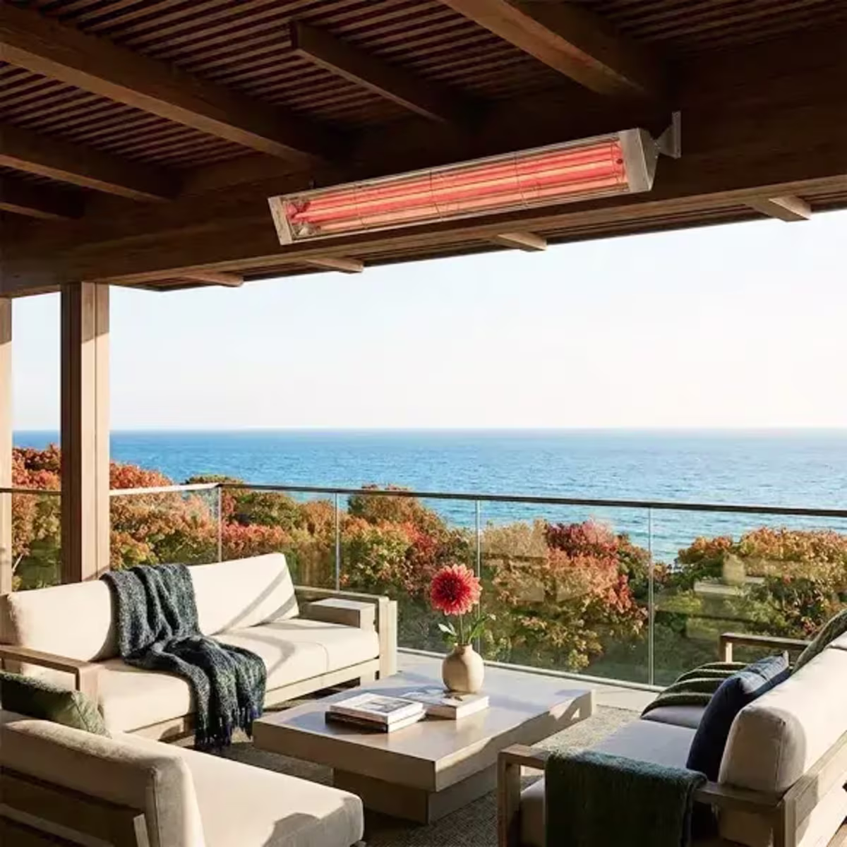 Ceiling-mounted patio heater above an outdoor lounge with sofas, blankets and an ocean view.