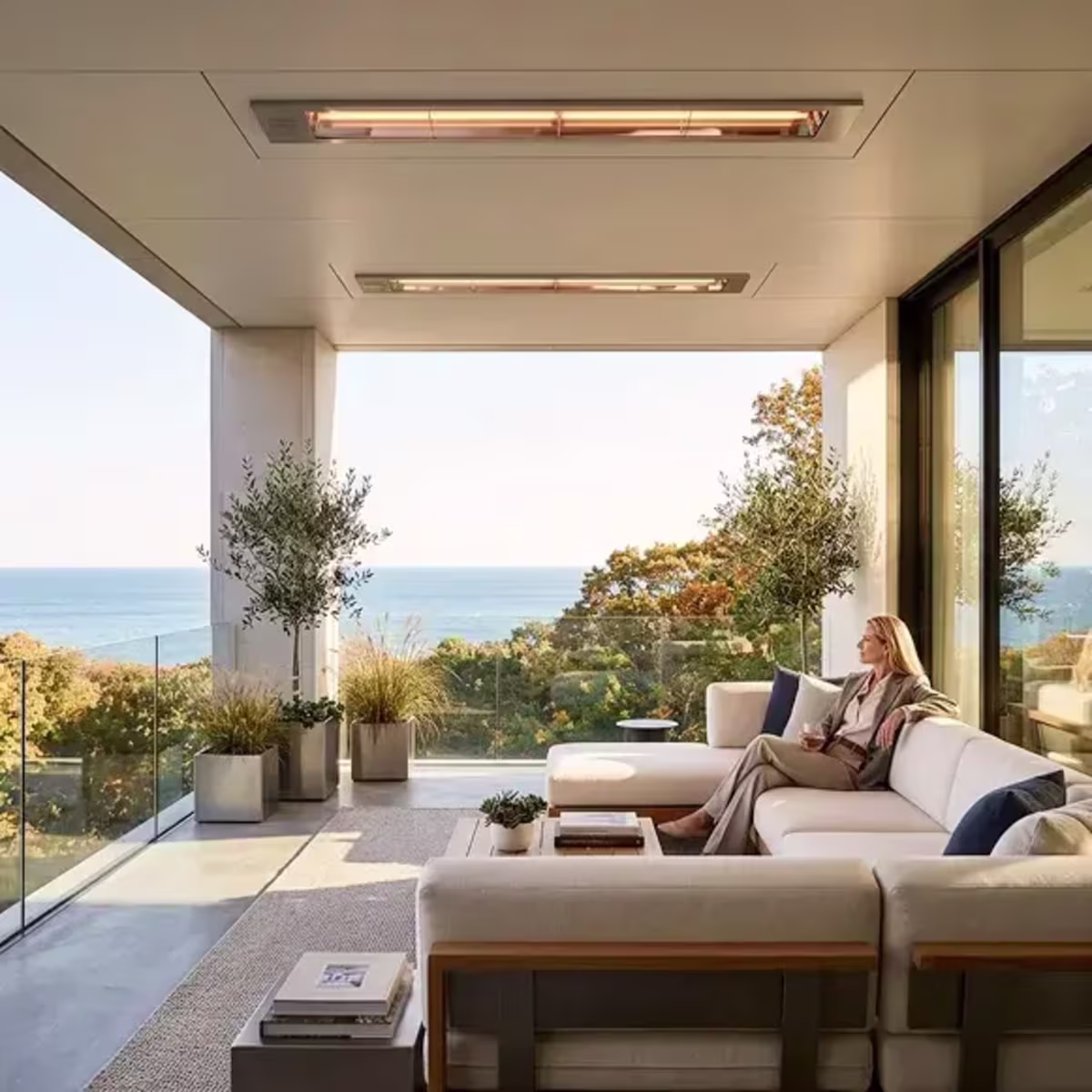 Recessed ceiling patio heaters above a sectional lounge with a woman seated overlooking the ocean.