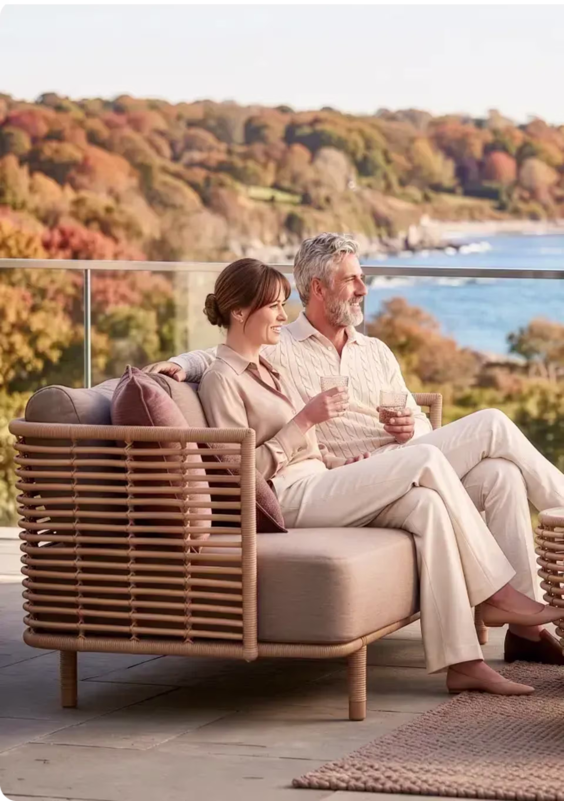 Couple relaxing together on a woven outdoor sofa with a fall coastal view.