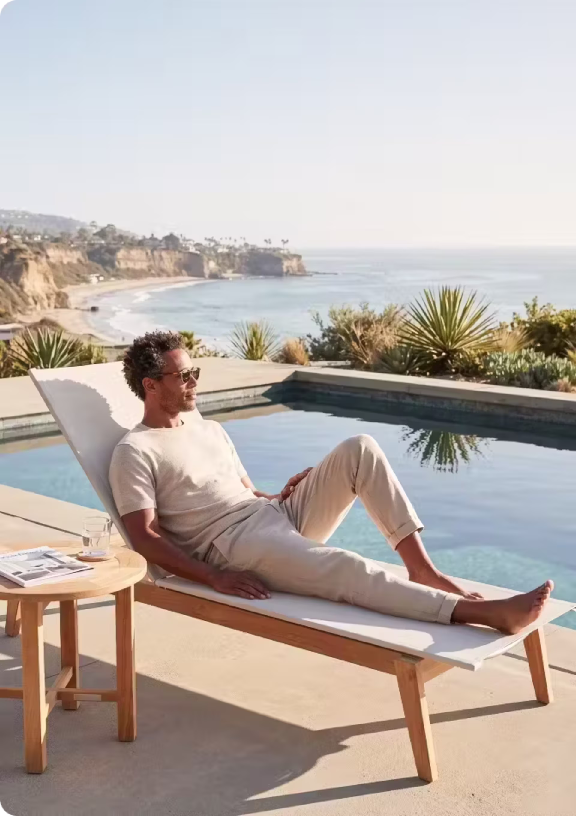Man relaxing on a contemporary chaise lounge beside a pool overlooking the ocean.