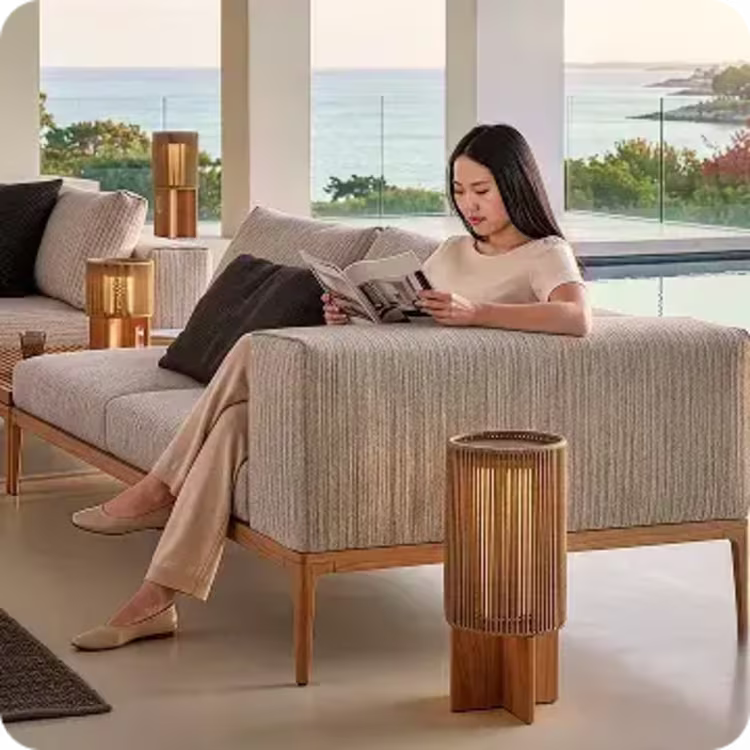 Woman reading on a modern outdoor sofa with decorative lanterns and ocean views.