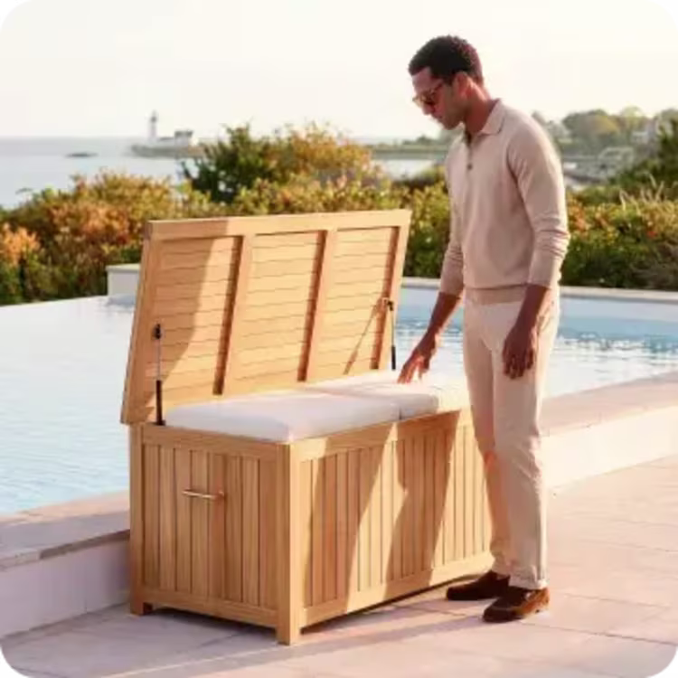 Man opening a teak outdoor storage box beside an infinity pool overlooking the coast.