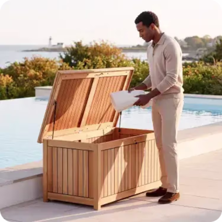 Man opening a teak outdoor storage box beside an infinity pool overlooking the coast.