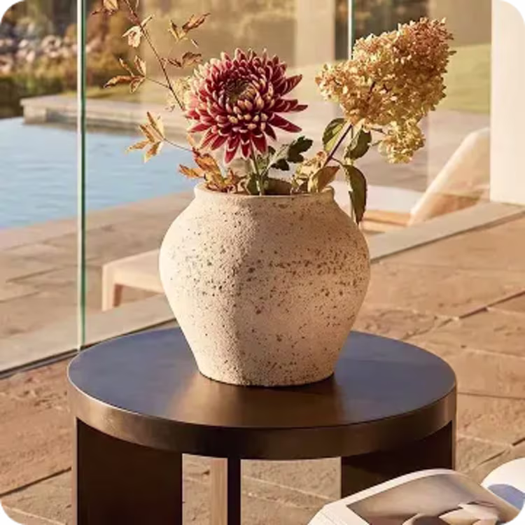 Ceramic vase with fresh flowers displayed on a round black outdoor side table.