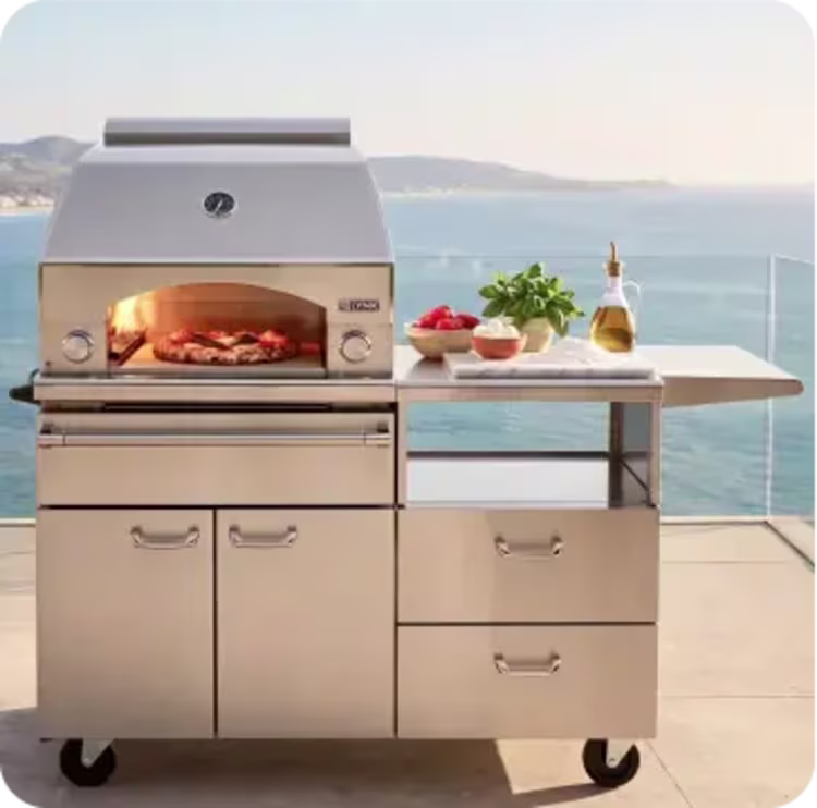 Image of an outdoor pizza oven and kitchen cart with fresh ingredients overlooking the ocean.