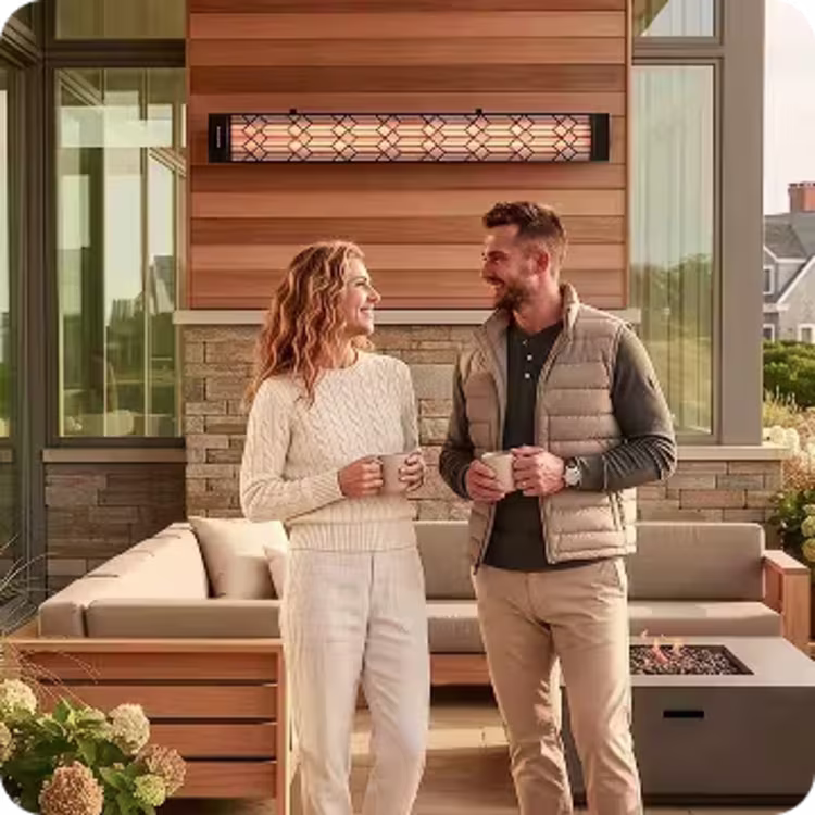 Couple holding mugs beneath a glowing wall-mounted patio heater beside an outdoor lounge.