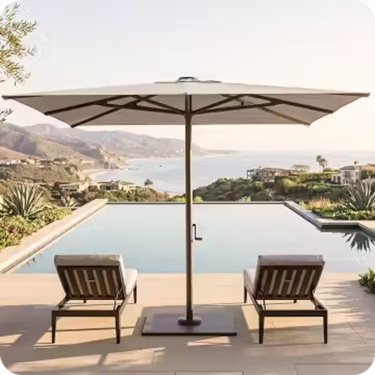 Two chaise lounges beneath a large market umbrella overlooking an infinity pool and the ocean.