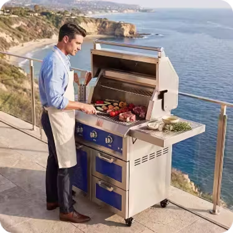 Man grilling food on a stainless steel outdoor grill overlooking the ocean from a contemporary patio.
