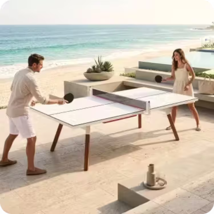 Man and woman playing table tennis on a contemporary outdoor patio overlooking the ocean.