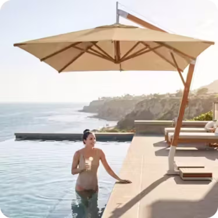 Woman relaxing in an infinity pool beneath a cantilever umbrella overlooking the ocean.