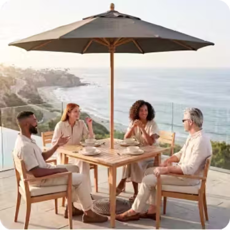 Four adults dining beneath a large market umbrella on a contemporary oceanfront patio.