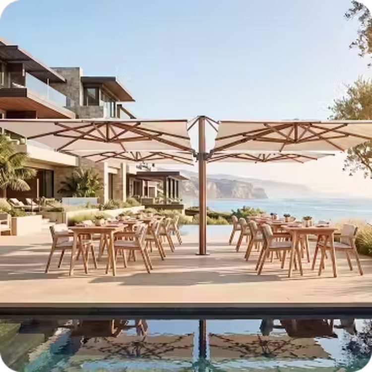 Commercial outdoor restaurant dining area with multiple tables shaded by large market umbrellas beside a pool overlooking the ocean.
