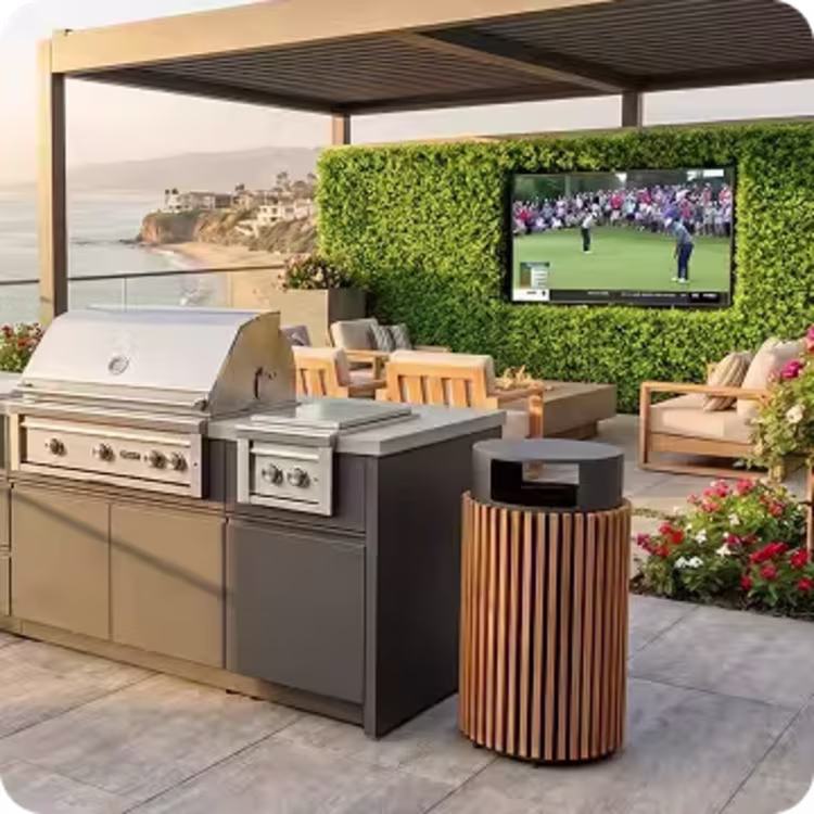 Contemporary outdoor kitchen with built-in grill, teak trash chute, seating area, and outdoor television overlooking the ocean.