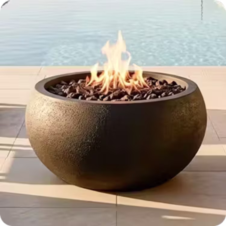 Round concrete gas fire bowl with flames beside a pool.