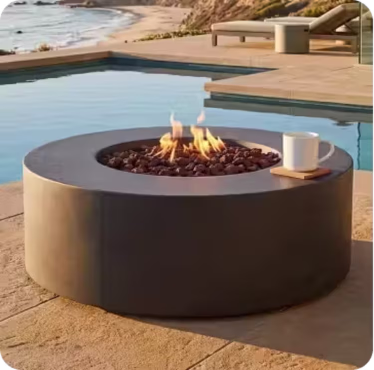 Round concrete gas fire table with flames beside a pool overlooking the ocean.
