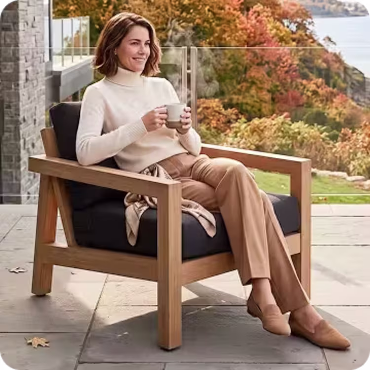 Woman holding a mug while relaxing in a cushioned teak outdoor lounge chair.