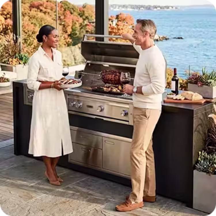 Couple preparing food at an outdoor grill overlooking the coast.
