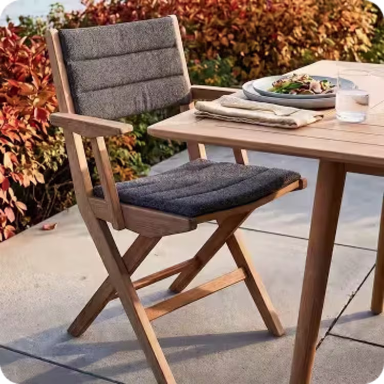 Cushioned teak folding dining chair beside a table set for a meal on an autumn patio.