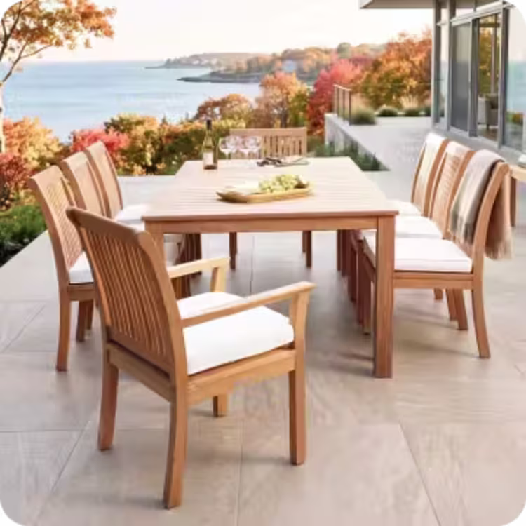 Teak outdoor dining table with cushioned chairs overlooking a colorful autumn coastline.