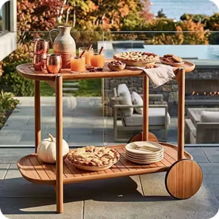 Teak serving cart holds drinks, pies and tableware on a coastal patio in autumn.