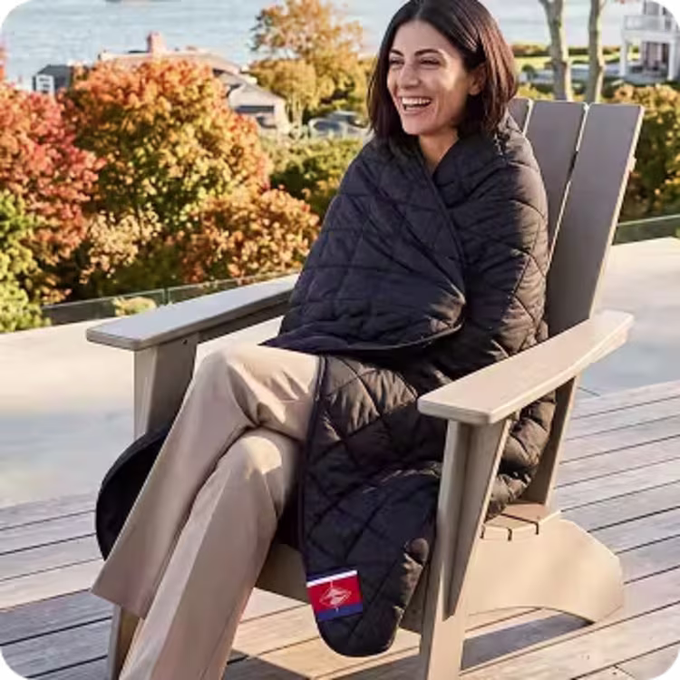 Woman relaxing in an outdoor chair wrapped in a black quilted blanket.