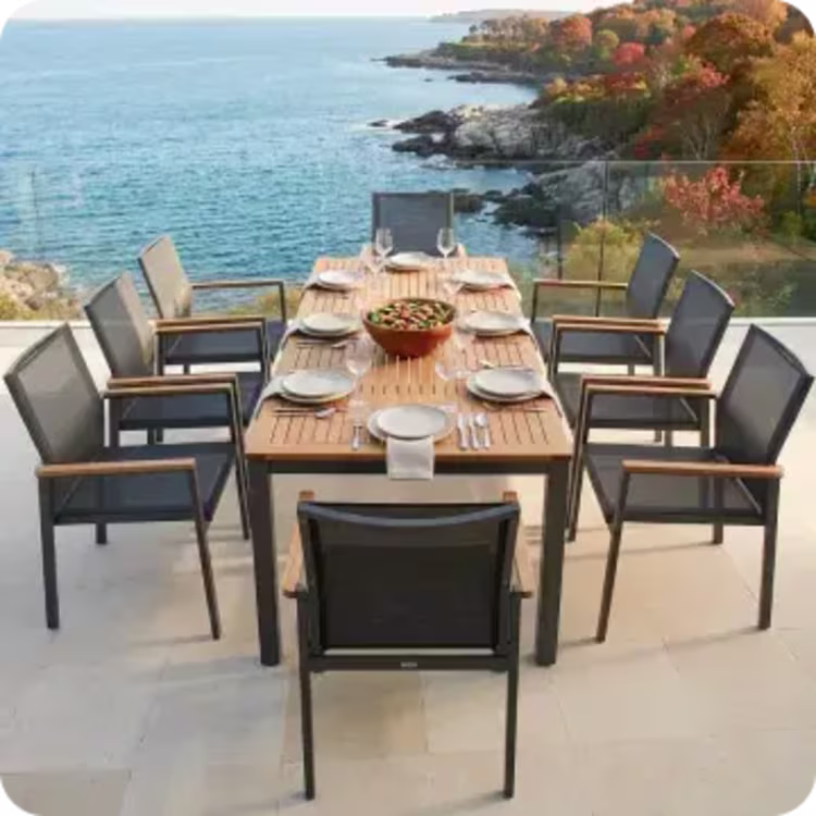 Teak dining table with six dark sling chairs set for a meal on a coastal patio.