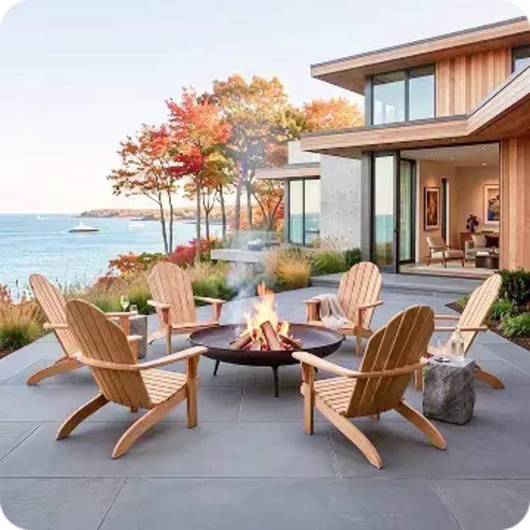 Adirondack chairs surround a glowing fire pit outside a modern coastal home in autumn.