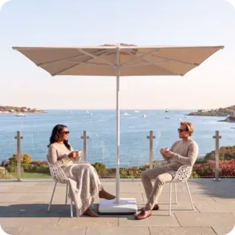Couple relaxing beneath a large patio umbrella overlooking the water.