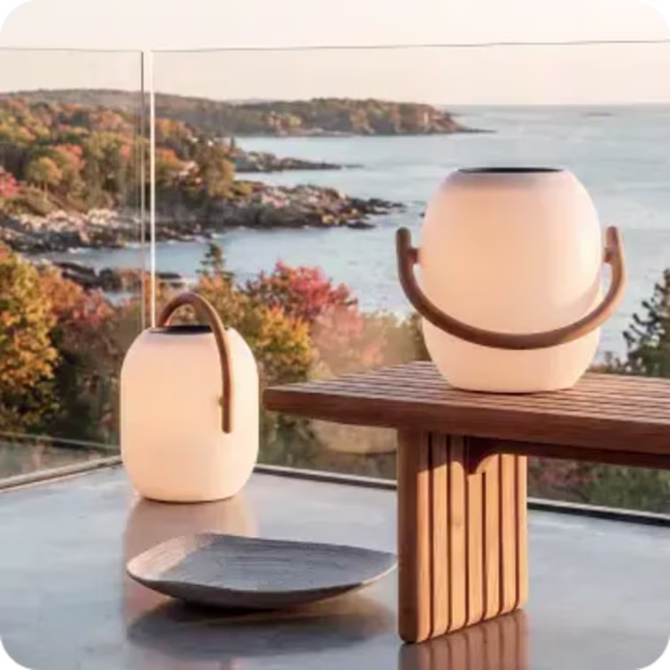 Modern outdoor lanterns displayed on a table overlooking a fall coastline.