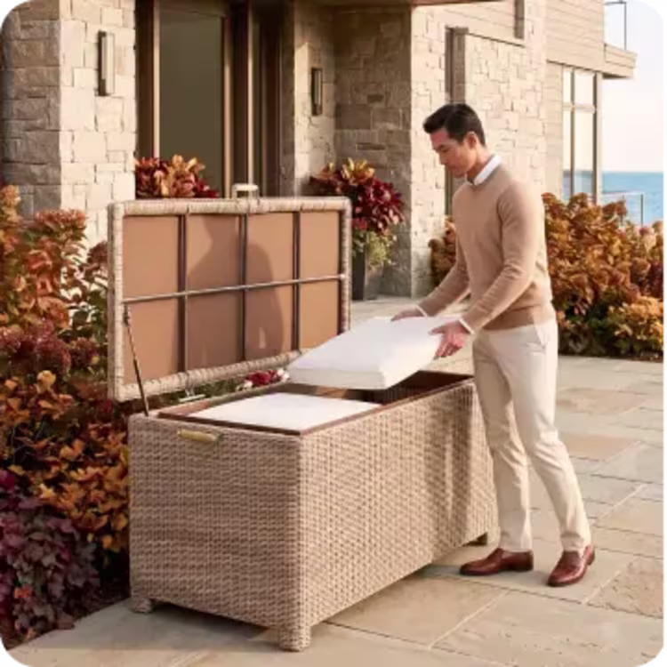 Man placing cushions inside a woven outdoor storage box on a fall patio.