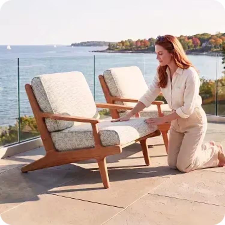 Woman arranging cushions on a lounge chair overlooking a fall coastline.