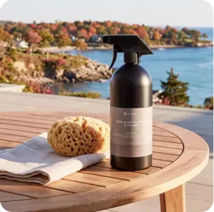 Outdoor furniture cleaner and sponge on a teak table with a fall coastal view.