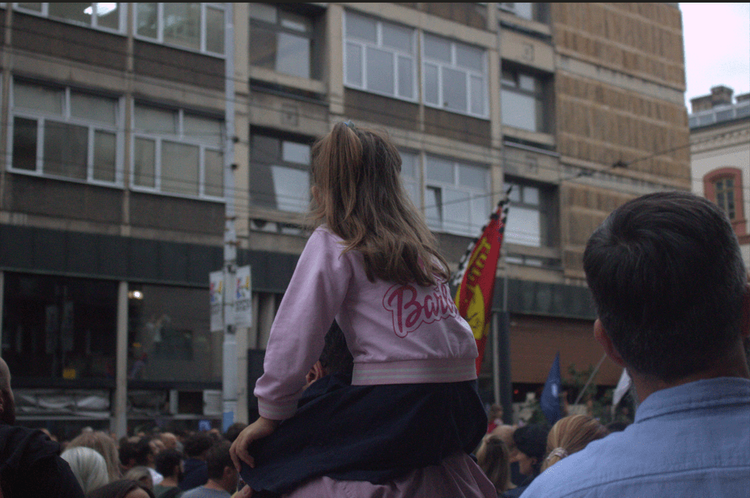 A child sitting on an adult’s shoulders among people gathered in front of the Rectorate in Belgrade