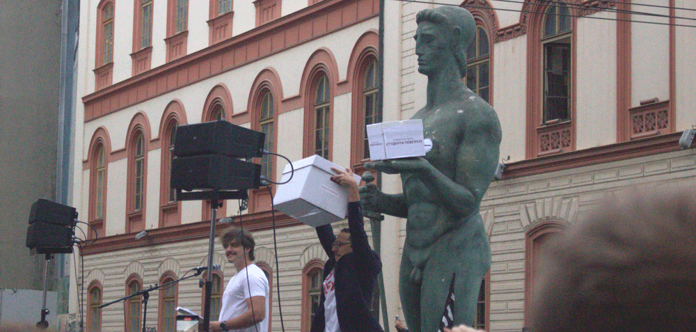 The student version of Pobednik with a “Students Win” box stands among the crowd in front of the Rectorate