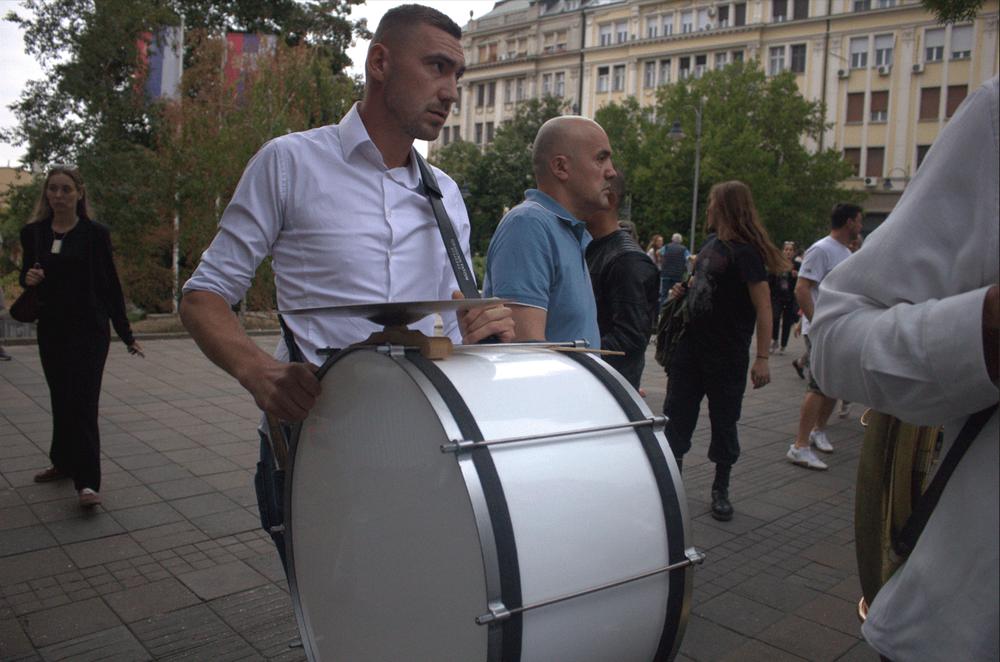 A musician with a large drum waits for the student procession outside the electoral commission building