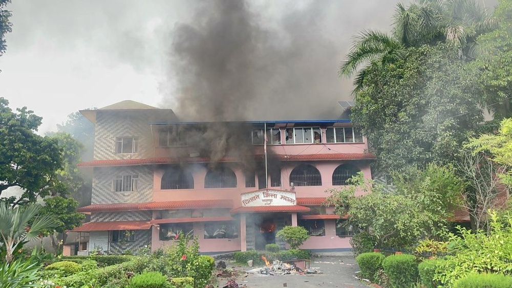 Nepal'deki Çitvan Bölge Mahkemesi binasından yoğun siyah duman yükseliyor; girişin önünde yangın izleri ve dağılmış eşyalar görülüyor.