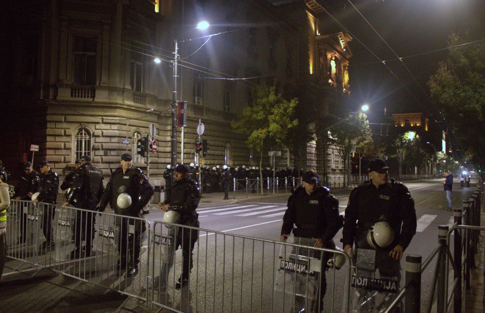 Αστυνομικοί πίσω από μεταλλικά κιγκλιδώματα σε φωτισμένο δρόμο τη νύχτα.