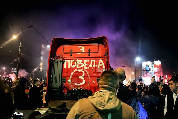 Το πίσω μέρος κόκκινου φορτηγού με «POBEDA» και μωβ καπνός πάνω από το πλήθος.