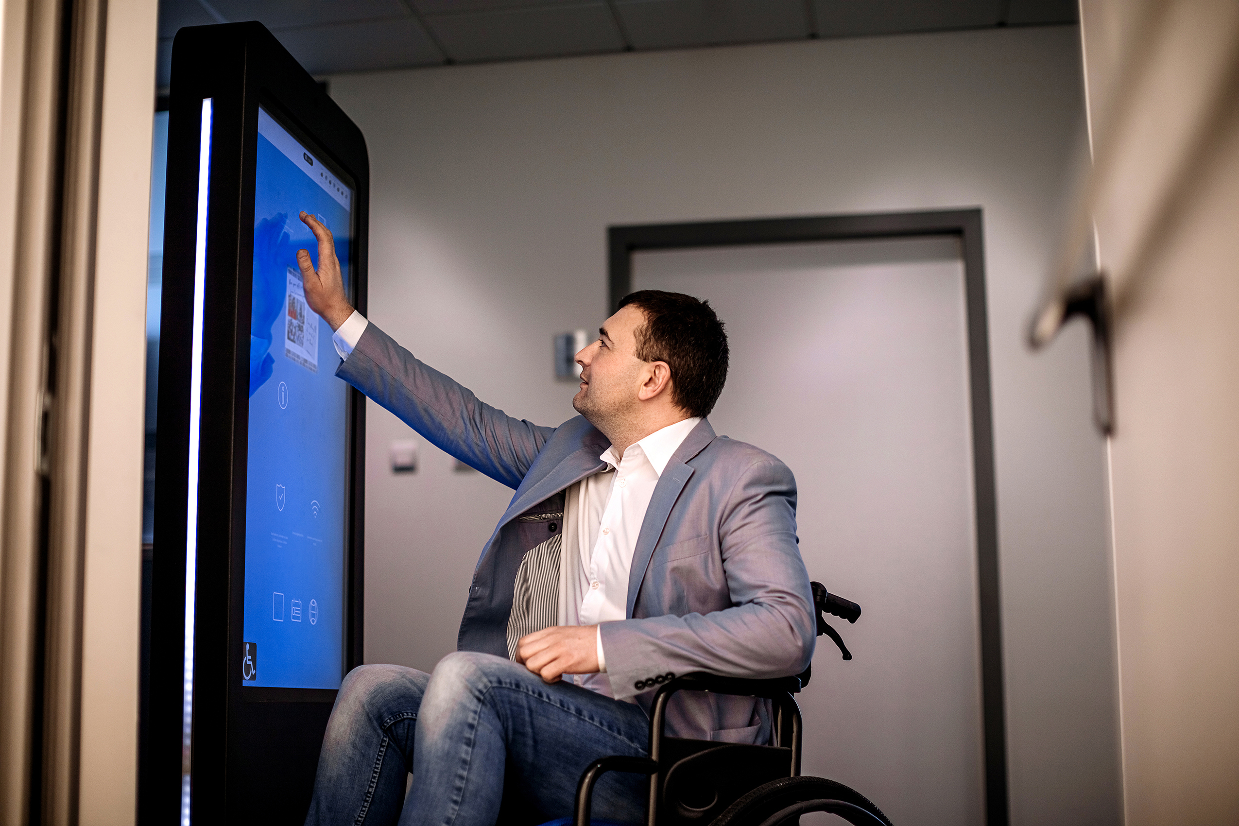 Man in wheelchair interacting with a digital signage kiosk.