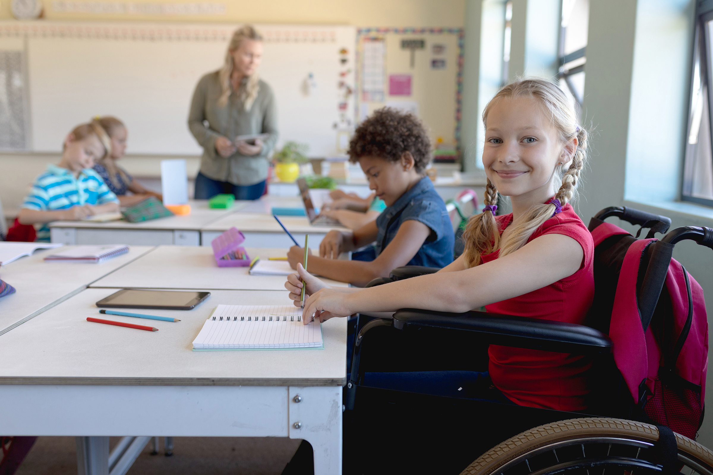 Girl in wheelchair at her desk space in an elementary classroom in session.