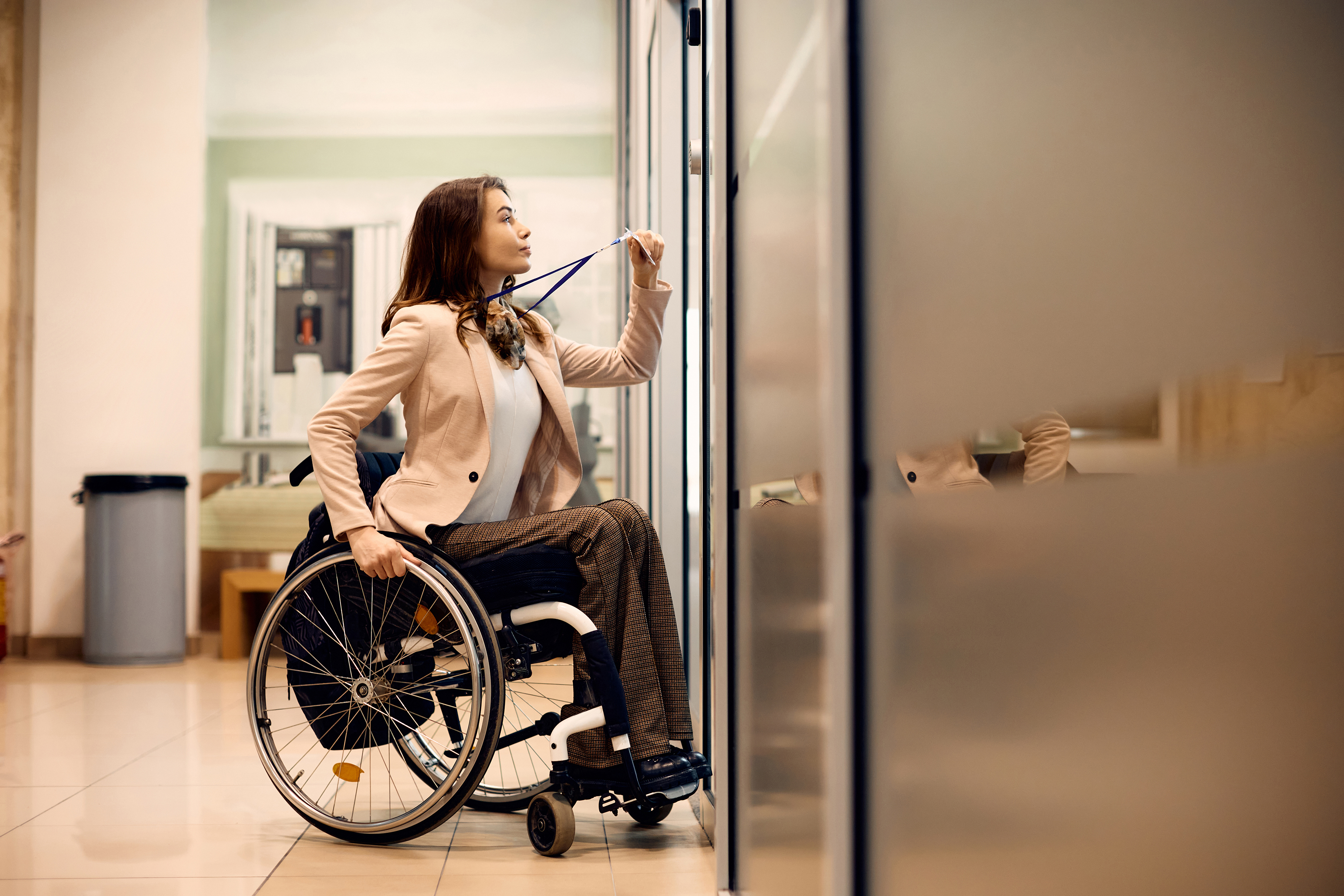 Woman in wheelchair using badge to gain entry to an office space.